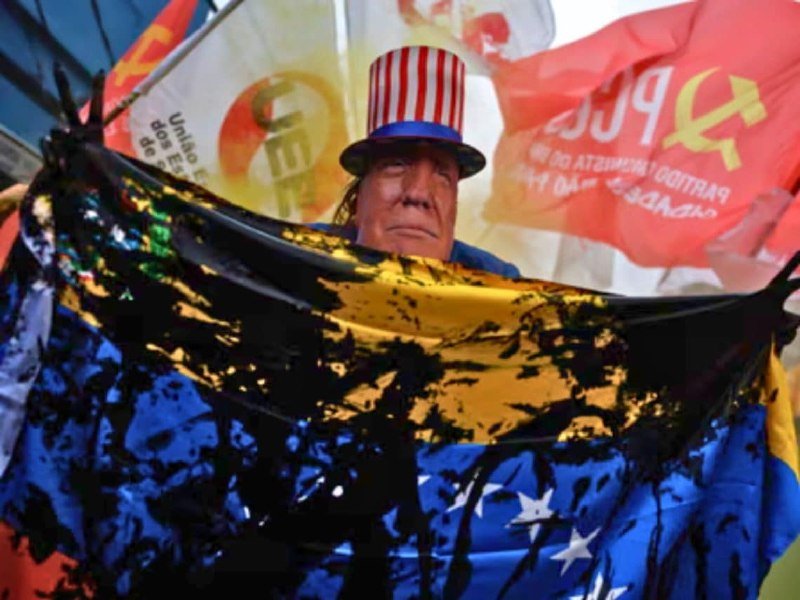 An effigy of a man wearing a striped top hat is surrounded by red flags and banners bearing communist symbols and partially legible Portuguese text, draped with a tarp.