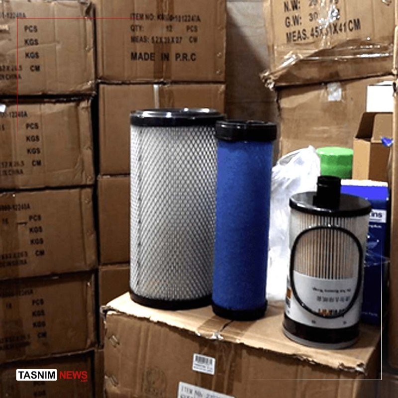 Cylindrical air and liquid filters sit atop stacked cardboard shipping boxes labeled "MADE IN P.R.C." in a warehouse setting, with a "TASNIM NEWS" watermark visible.