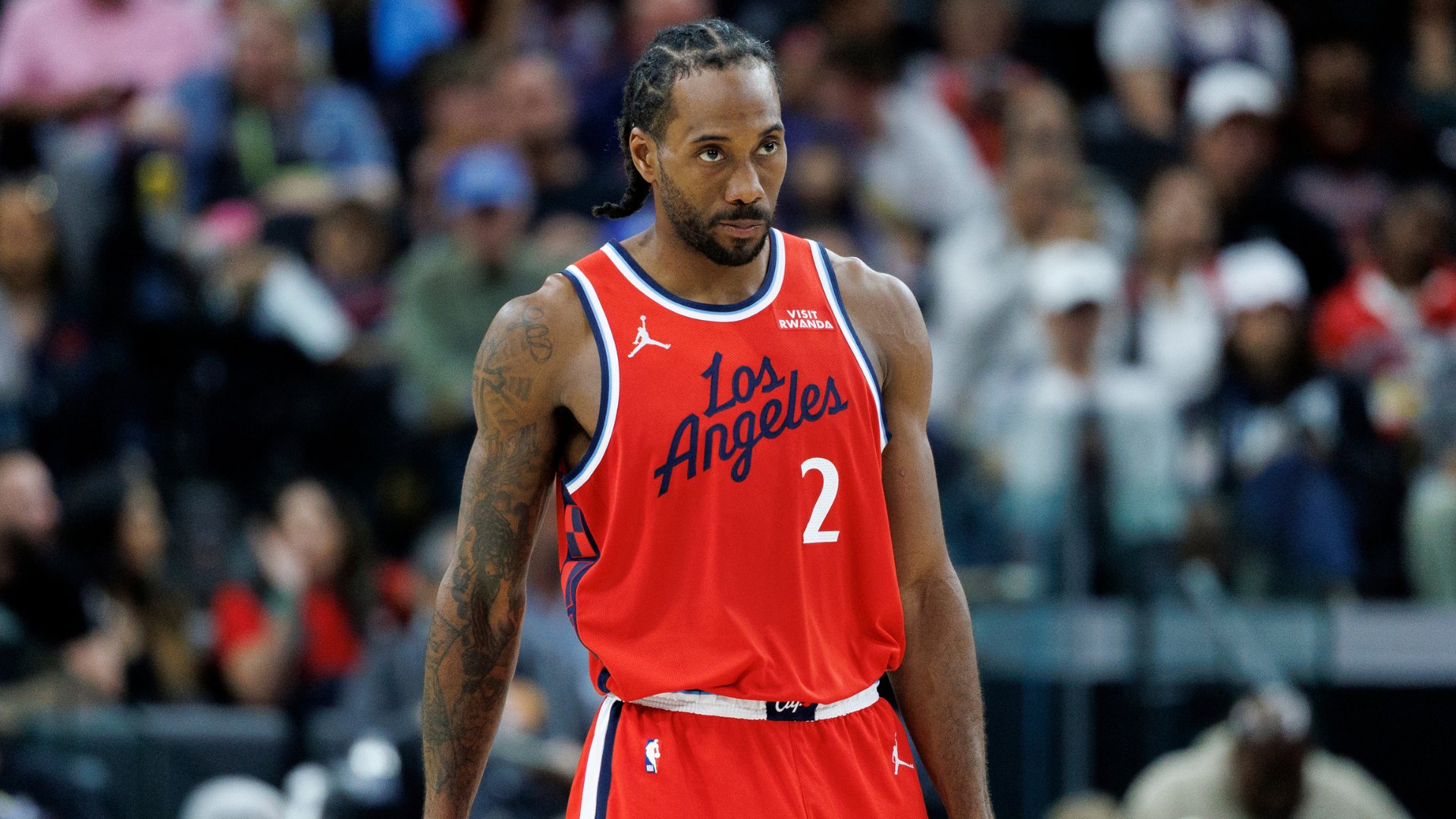 A basketball player wearing a red "Los Angeles" jersey with the number 2 stands on the court, with a blurred crowd visible in the background.